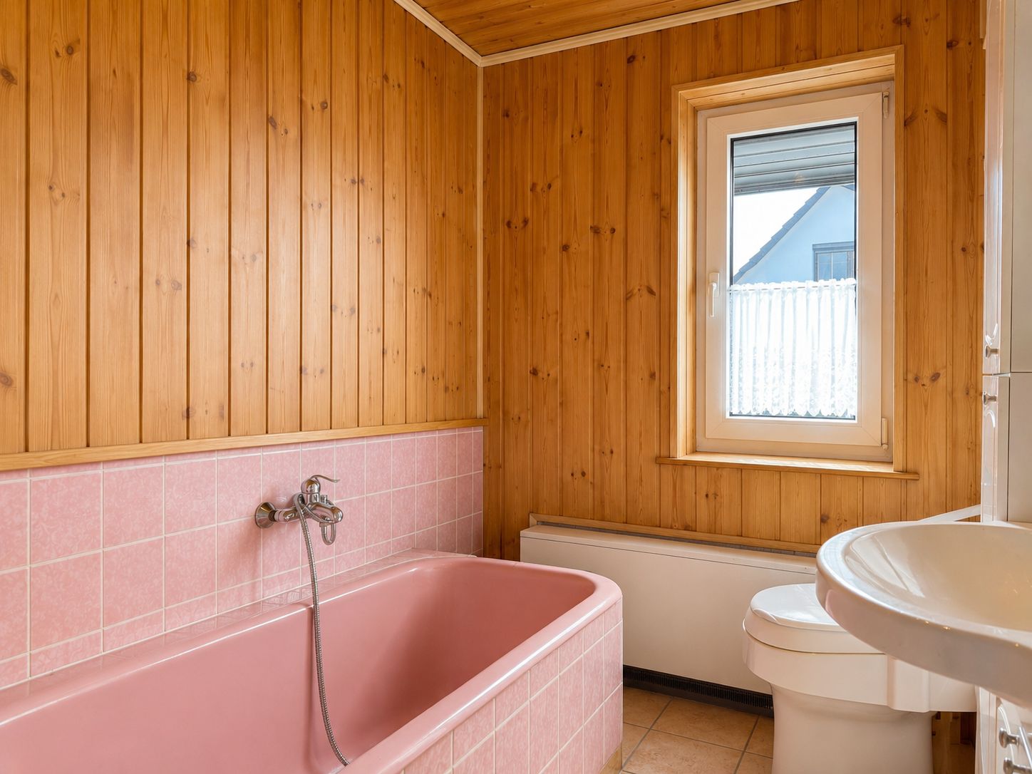 Badezimmer mit rosa Badewanne, Holzvertäfelung und Fenster.
