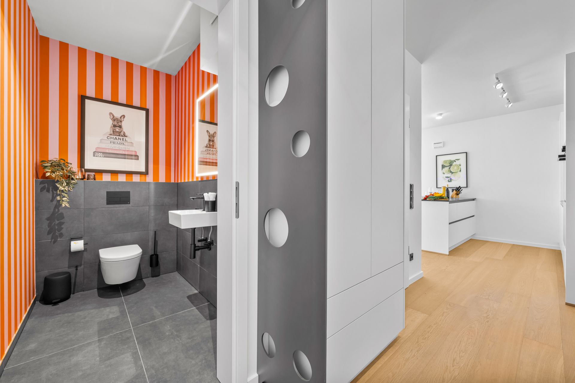 Modernes Badezimmer mit orange-weiß gestreifter Wand, WC, Waschbecken und Wandbild.