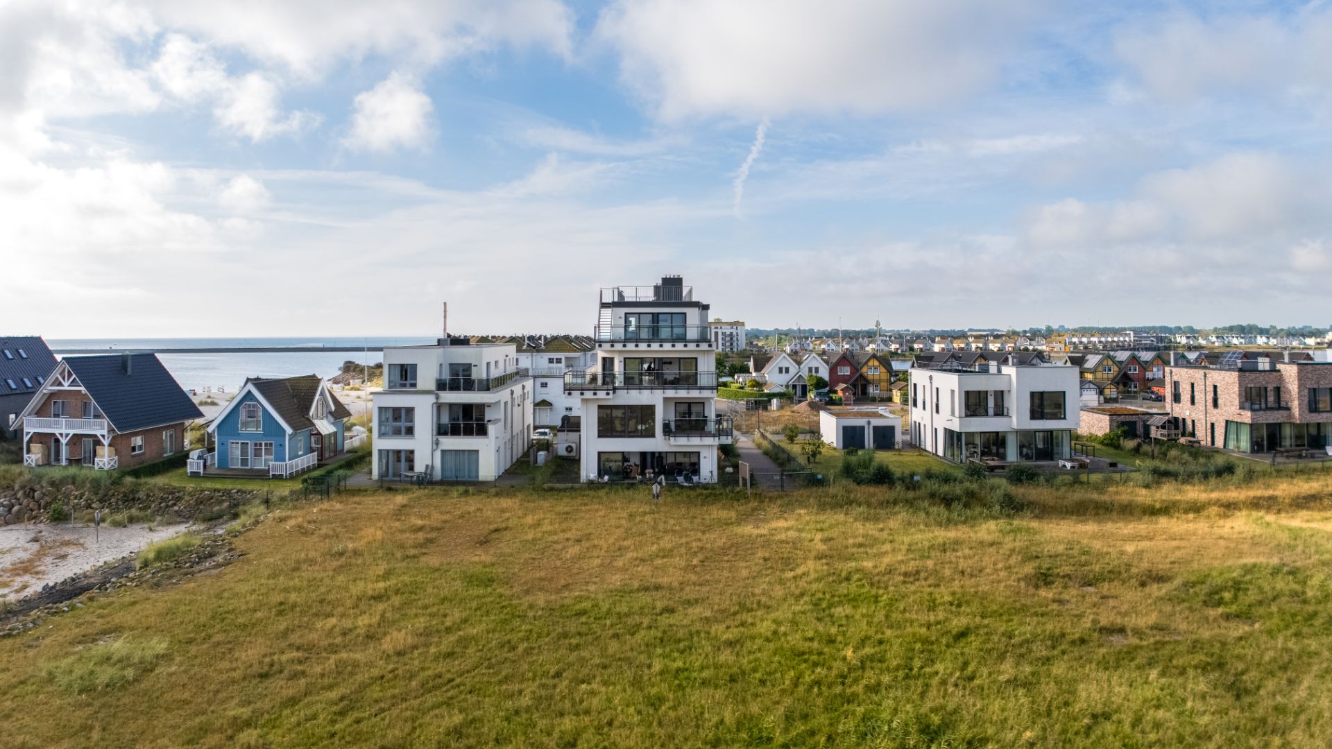 Mehrere moderne Wohnhäuser mit Flachdach und große Fenster stehen auf einer Wiese nahe dem Wasser.
