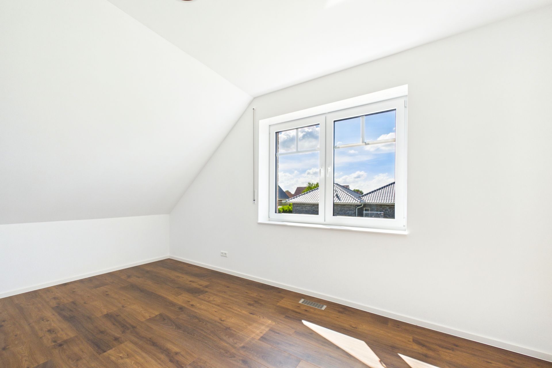 Helles Zimmer mit weißer Wand, Holzfußboden und Fenster mit Blick nach draußen.