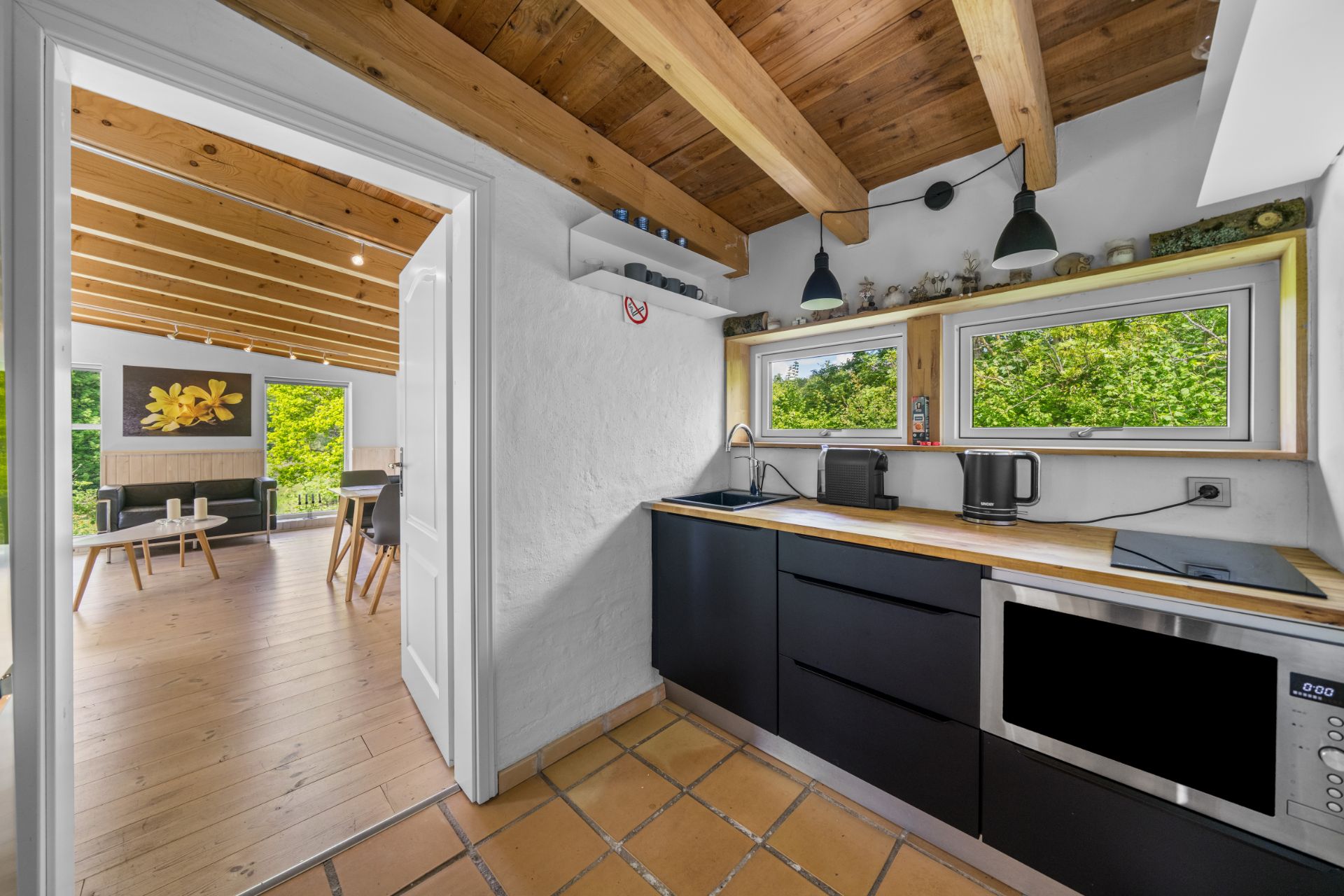 Moderne Küche mit Holzbalkendecke, schwarzen Schränken und Blick ins Wohnzimmer.