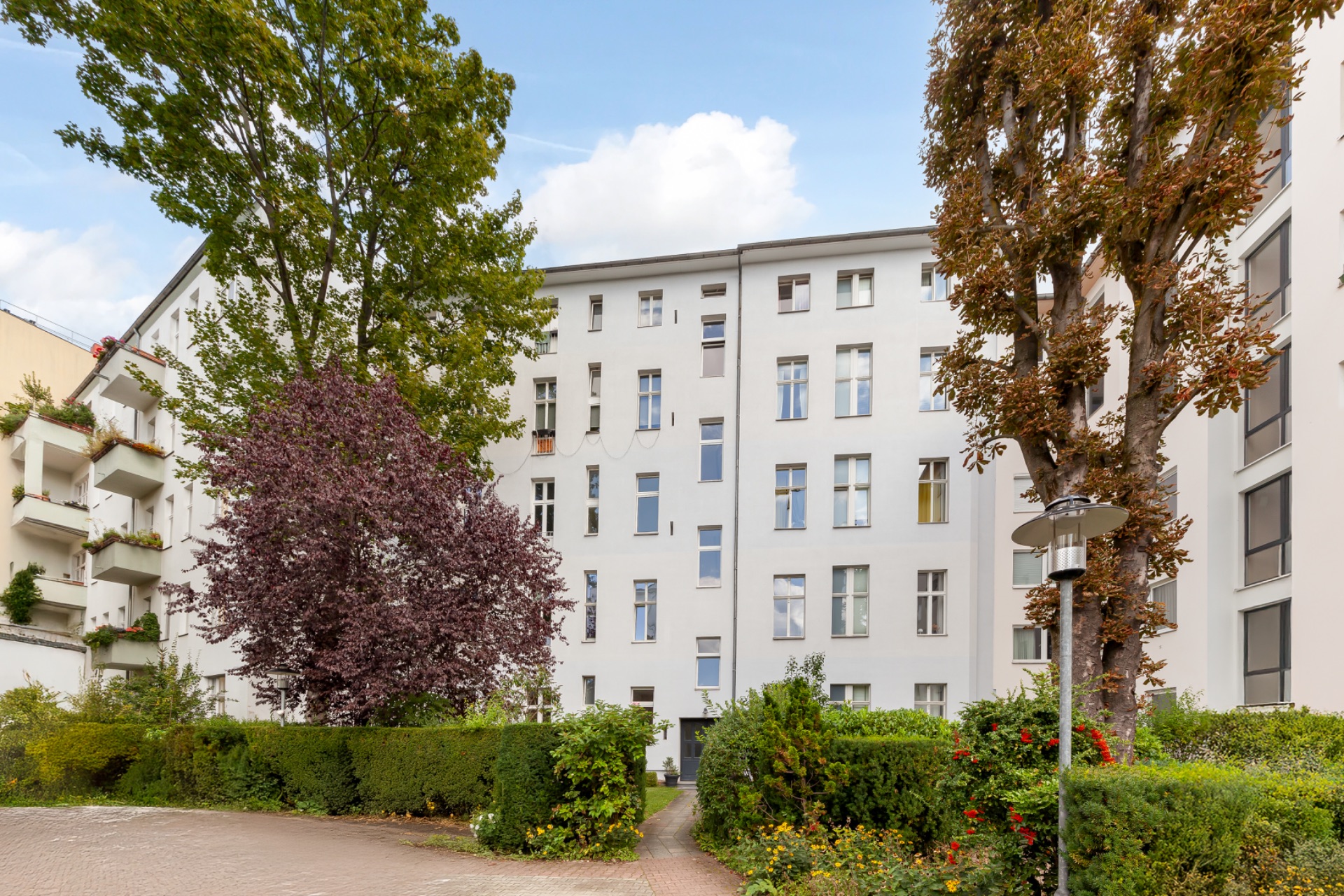 Mehrstöckiges Wohnhaus mit hellen Fassaden, umgeben von Bäumen und gepflegten Grünanlagen.