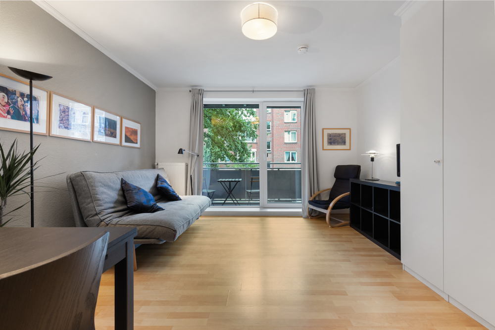 Modernes Wohnzimmer mit Schlafsofa, Sessel, Regal und Zugang zu einem Balkon.