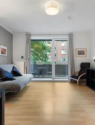 Modernes Wohnzimmer mit Schlafsofa, Sessel, Regal und Zugang zu einem Balkon.