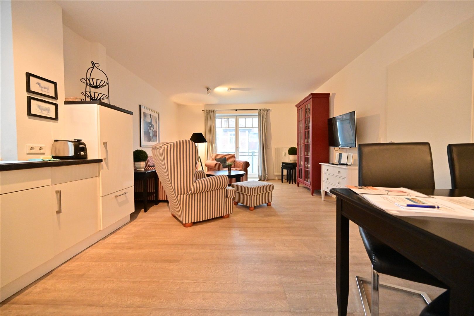 Helles Wohnzimmer mit Sesseln, Esstisch, Schrank, Fernseher und Küchenzeile.