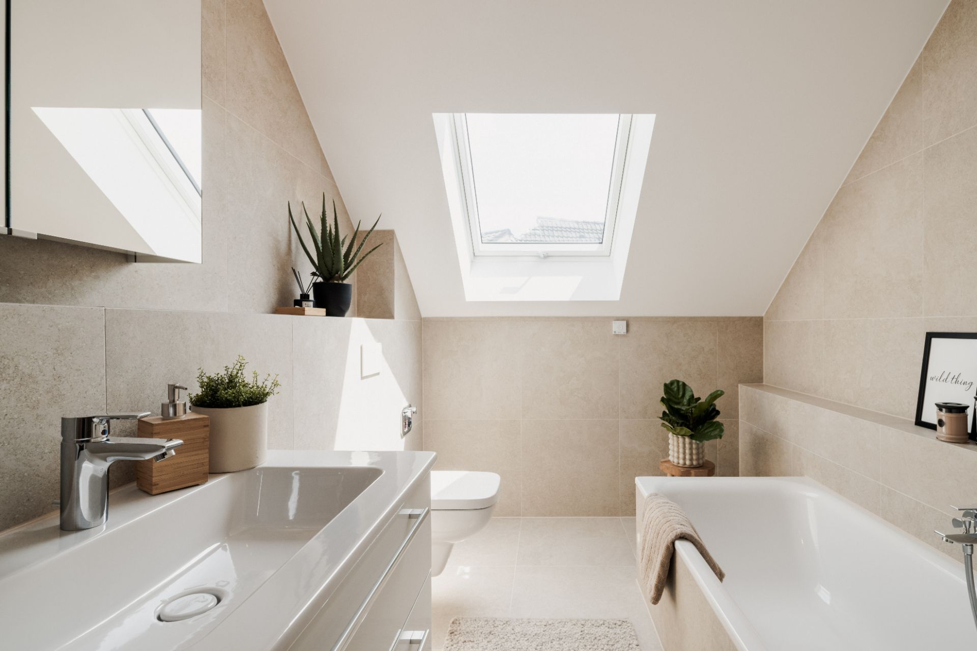 Modernes Badezimmer mit Badewanne, Waschbecken, Toilette und Dachfenster, dekoriert mit Pflanzen.