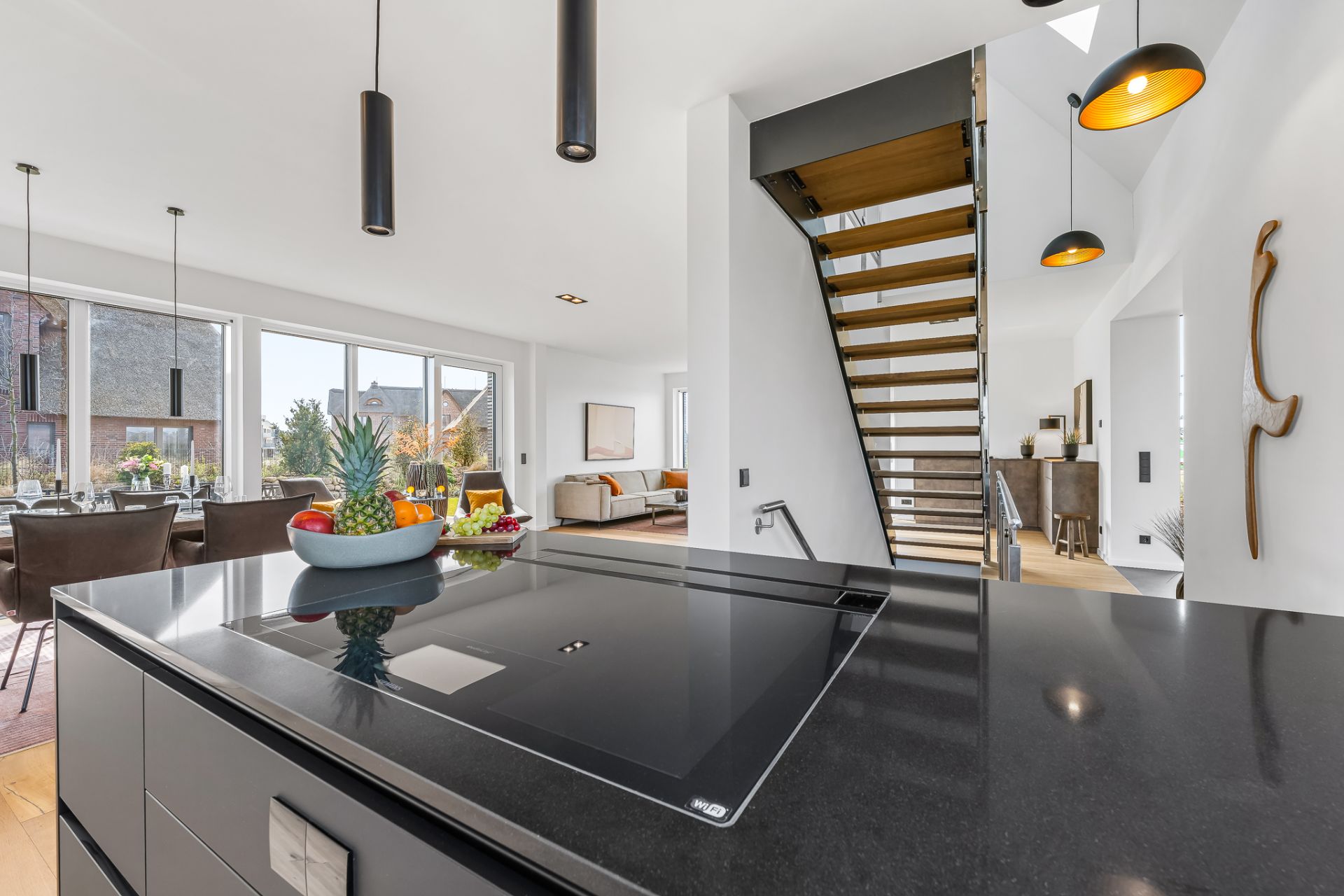 Moderne offene Küche mit Kochinsel, Holztreppe und Essbereich mit großen Fenstern.