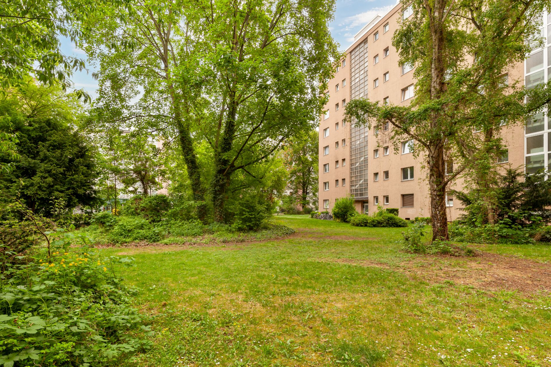 Grüner Innenhof mit Rasen, Bäumen und mehrstöckigem Wohngebäude im Hintergrund.