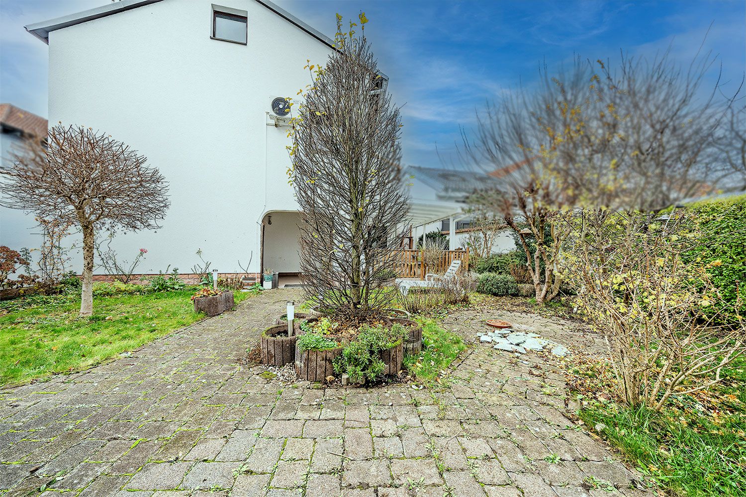 Gepflasterter Gartenweg mit Bäumen und Sträuchern neben einem weißen Wohnhaus.