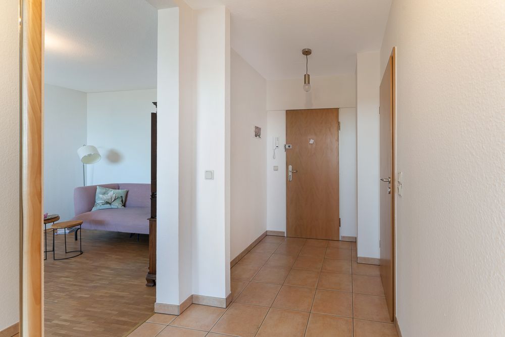 Flur mit Fliesenboden und Holztür, Blick ins Wohnzimmer mit Sofa und Lampe.