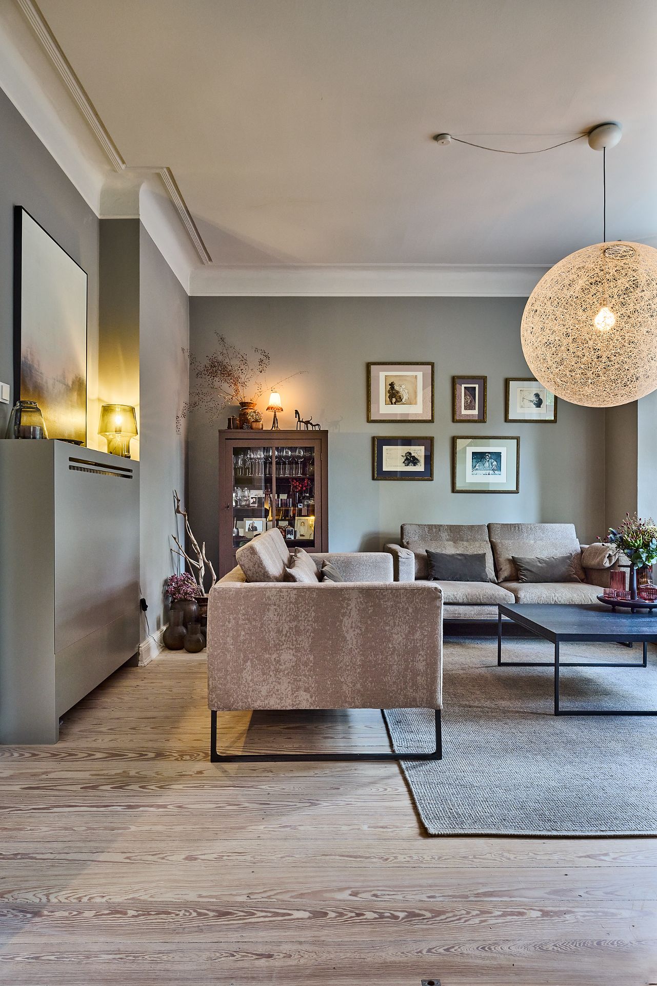 Modernes Wohnzimmer mit beigen Sofas, Holzboden, großem Teppich und dekorativer Hängelampe.