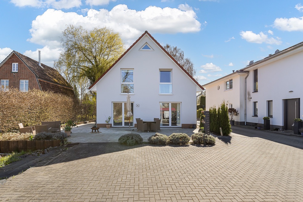 Modernes weißes Einfamilienhaus mit Terrasse und Gartenmöbeln, gepflasterter Hof im Vordergrund.