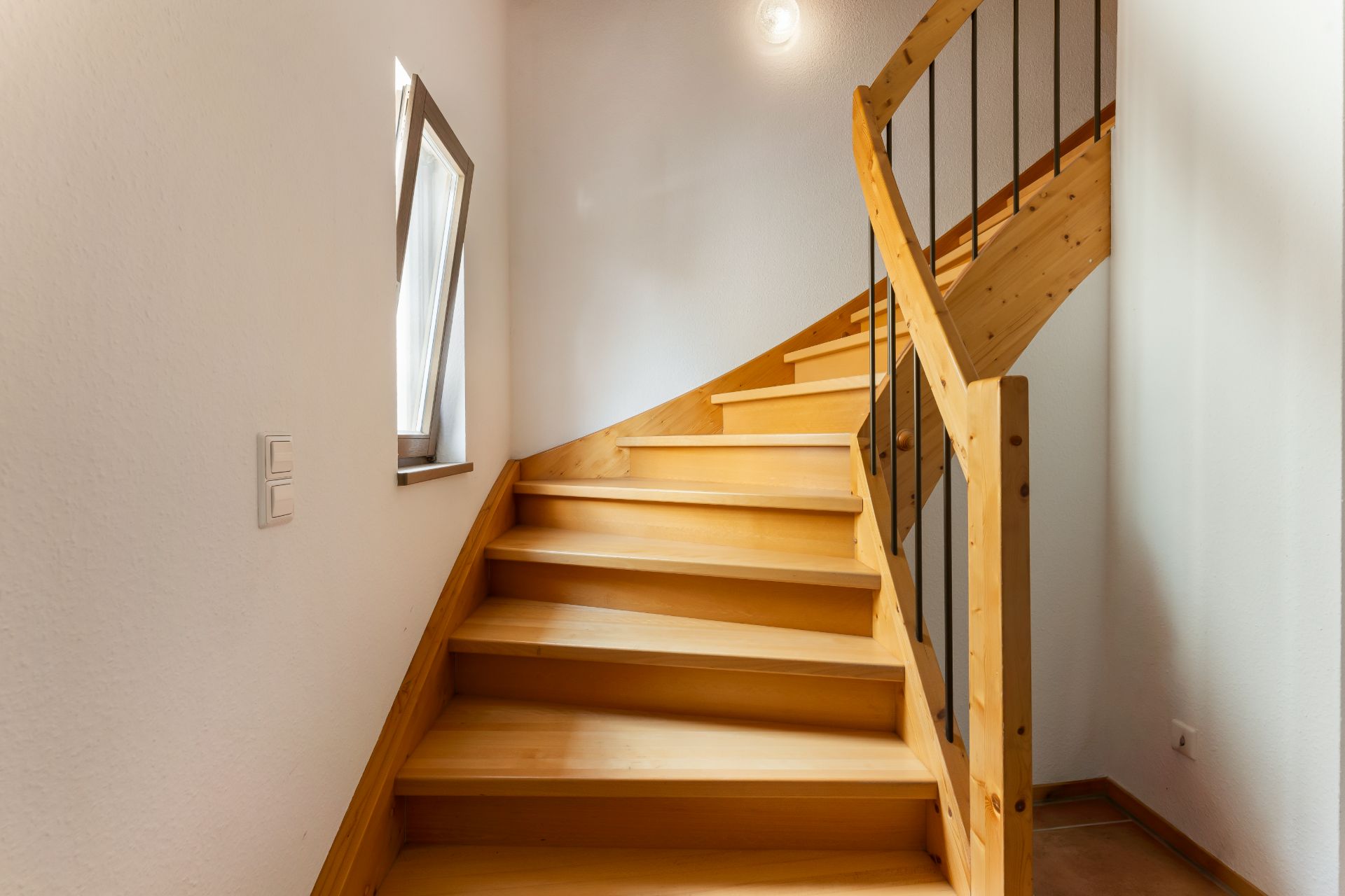 Hölzerne Wendeltreppe mit Geländer und kleinem Fenster an der Wand.