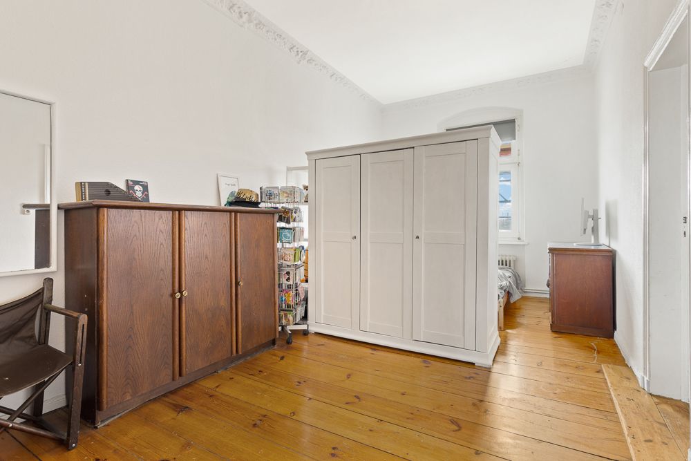 Helles Zimmer mit Holzboden, zwei Schränken und einem Stuhl an der Wand.