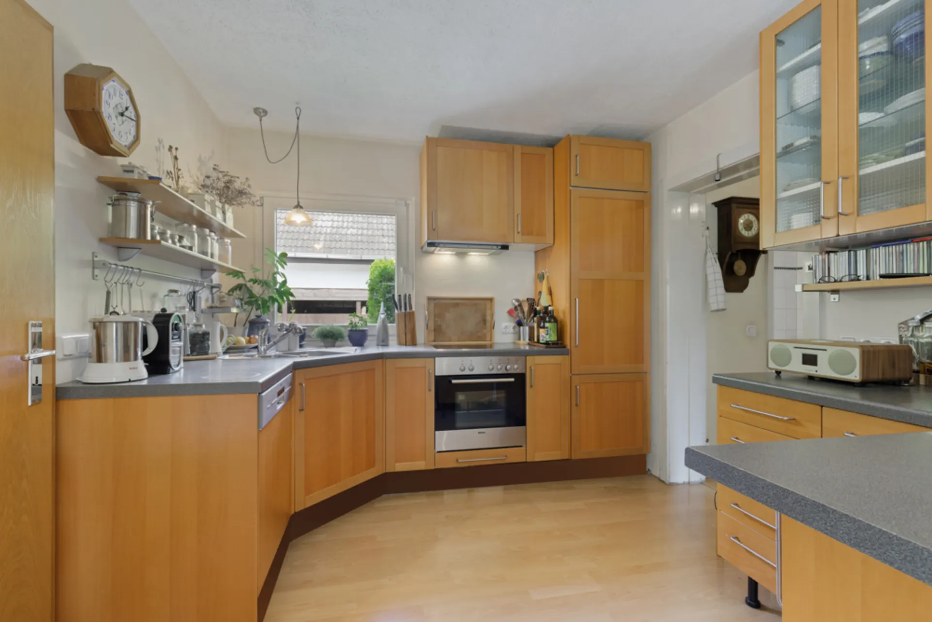 Helle Küche mit Holzfronten, Küchengeräten, Regal und Fensterausblick auf den Garten.