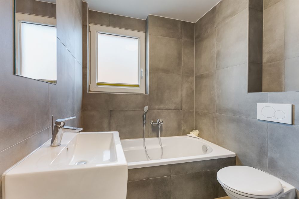 Modernes Badezimmer mit Badewanne, Waschbecken, Toilette und zwei Fenstern.