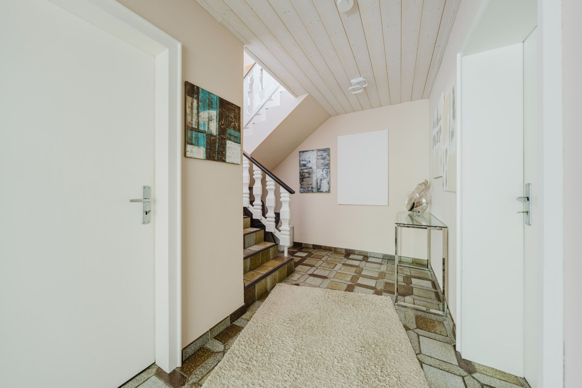Heller Flur mit Teppich, Fliesenboden, Treppe nach oben und Wandbildern.