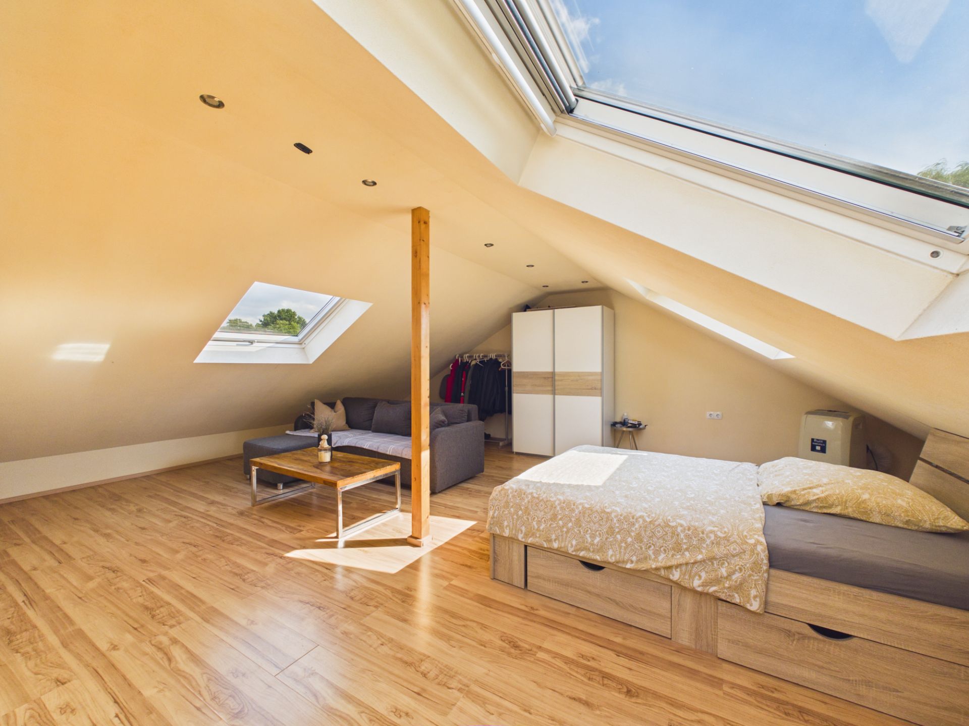 Helles Dachzimmer mit Bett, Sofa, Kleiderschrank und großen Dachfenstern.