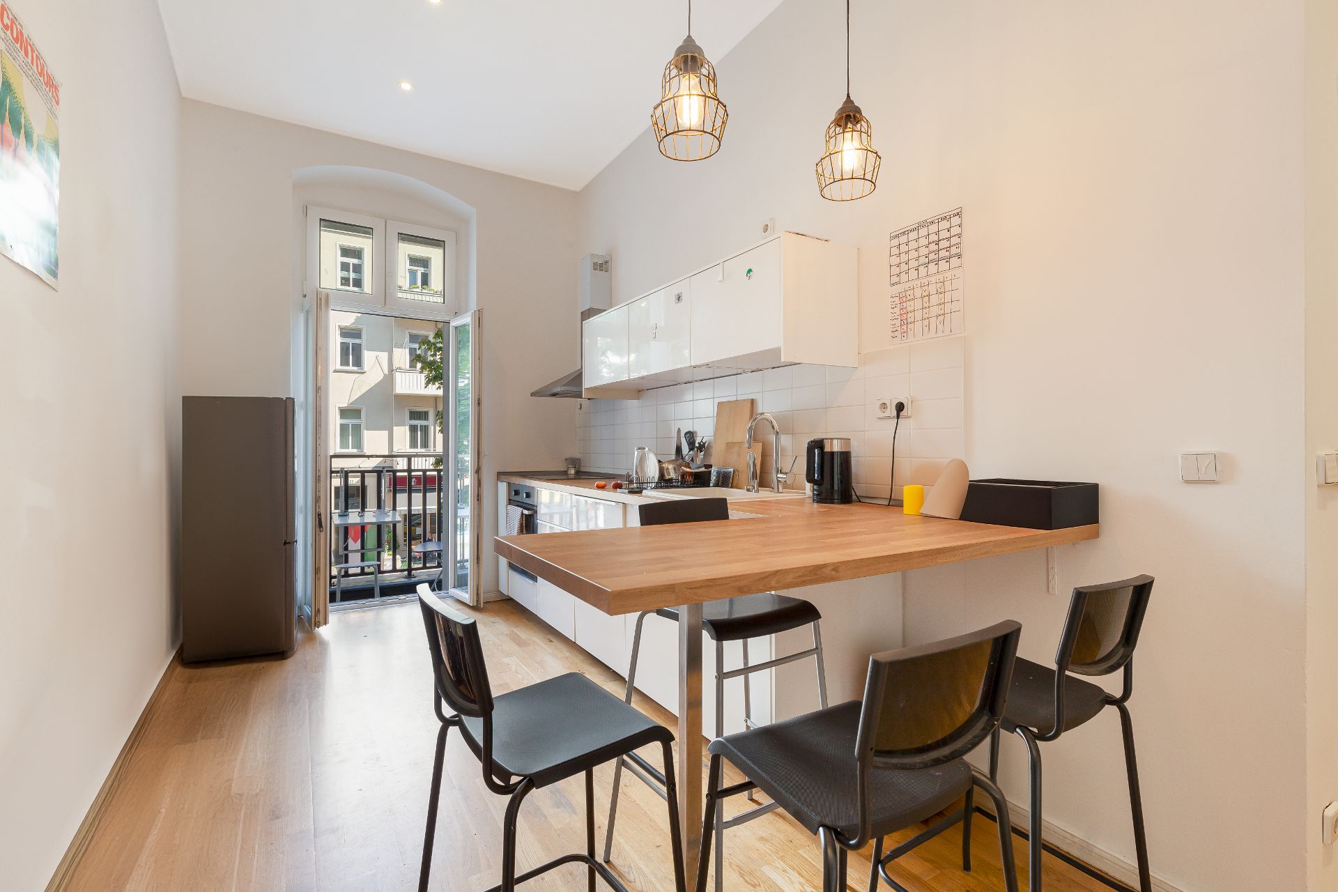 Helle Wohnküche mit Holztisch, Stühlen, Küchenzeile und offenem Fenster zum Balkon.