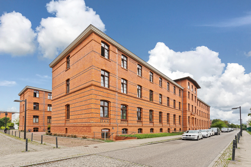 Großes Wohngebäude aus rotem Backstein an einer ruhigen Straße mit parkenden Autos.