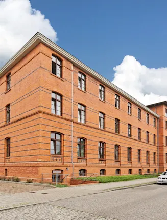 Großes Wohngebäude aus rotem Backstein an einer ruhigen Straße mit parkenden Autos.