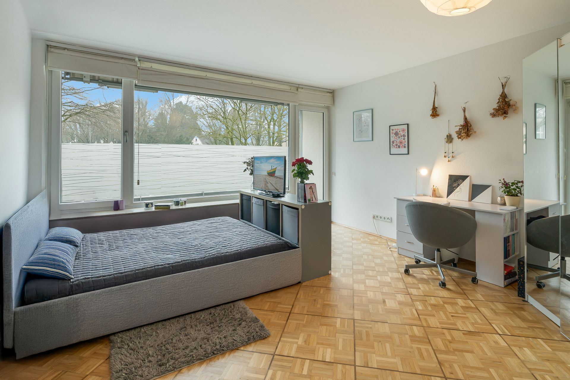 Modernes Schlafzimmer mit großem Fenster, Bett, Teppich, TV, Schreibtisch und Dekoration an der Wand.