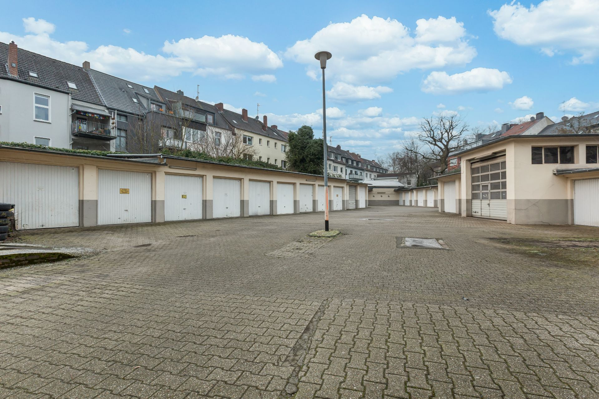 Gepflasterter Hof mit mehreren Garagen und Laterne, umgeben von Wohnhäusern.