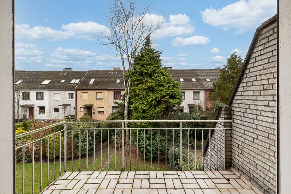 Aussicht von einem Balkon auf einen Garten und Reihenhäuser mit Bäumen und Sträuchern.