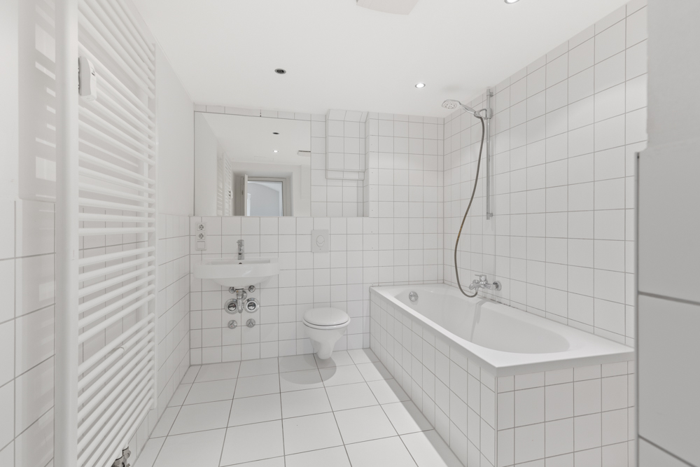 Helles Badezimmer mit Badewanne, Waschbecken, WC und weiß gefliesten Wänden.