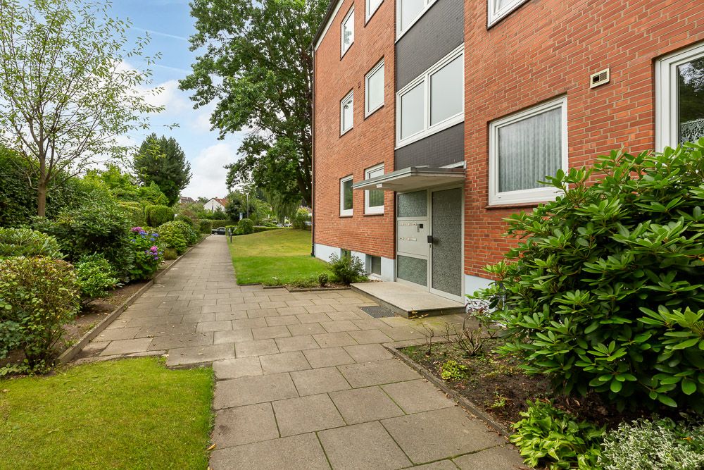 Eingang eines Mehrfamilienhauses mit Gehweg und grüner Bepflanzung davor.