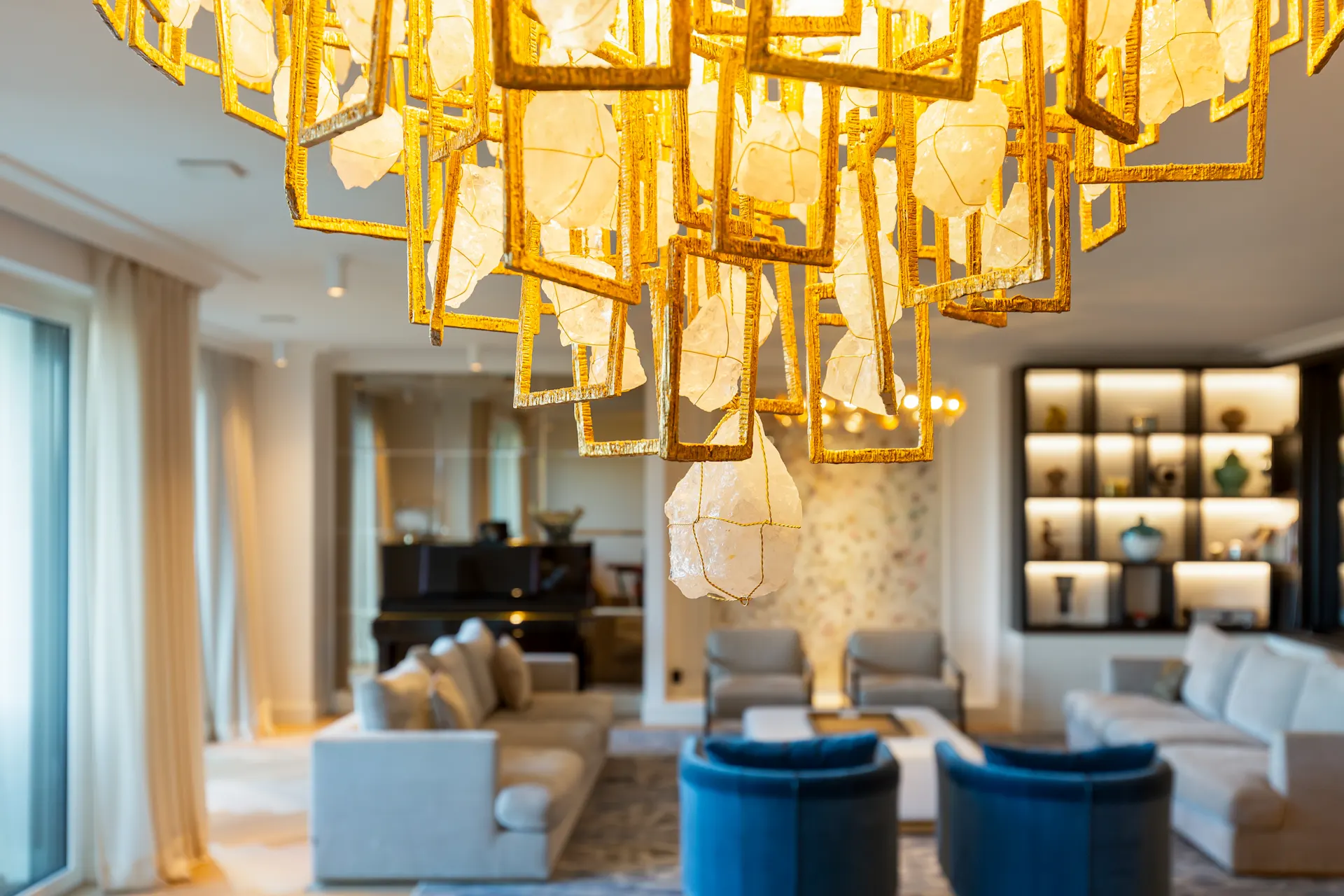 Wohnzimmer mit modernen Sofas, blauem Sessel und auffälligem, goldenem Kronleuchter.