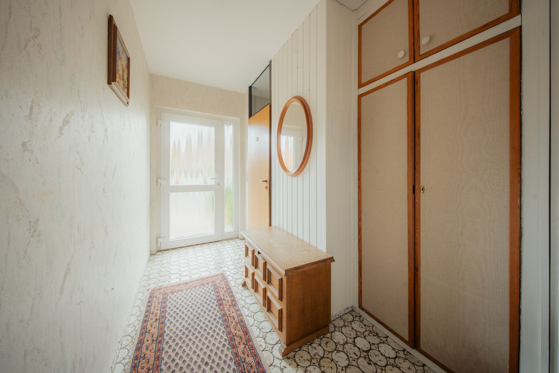 Heller Flur mit Teppich, Holzbank, rundem Spiegel und Einbauschrank.
