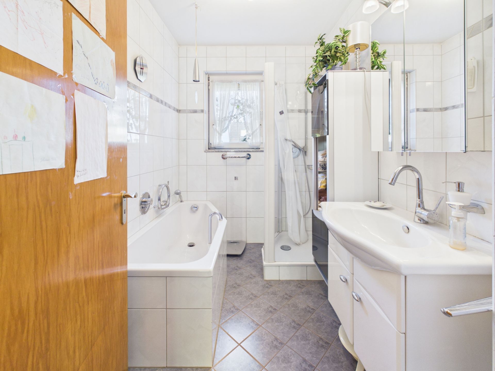 Helles Badezimmer mit Badewanne, Dusche, Doppelwaschbecken und weißen Fliesen.
