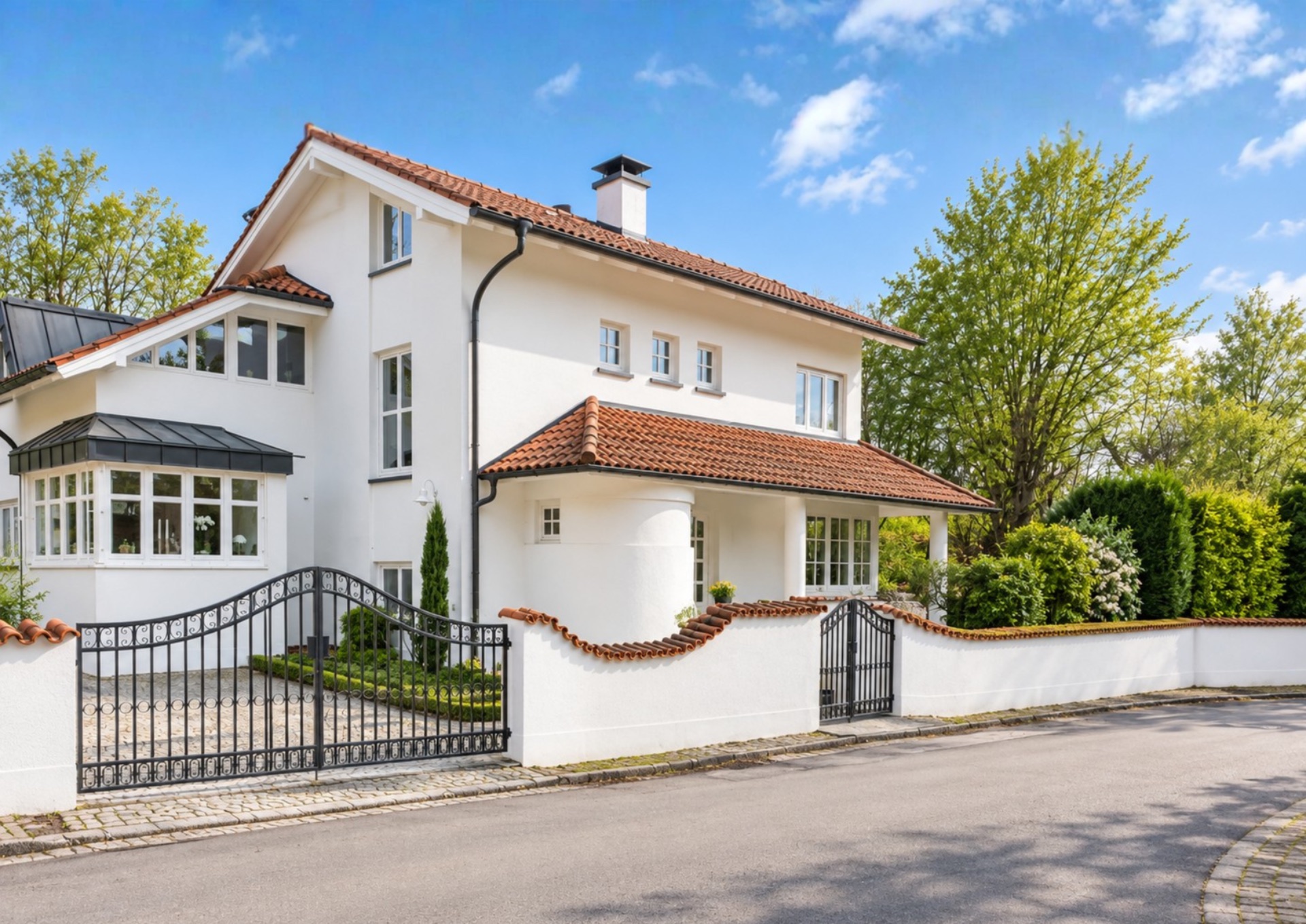 Weißes Einfamilienhaus mit rotem Dach und Garten, umgeben von einem Zaun mit Tor.