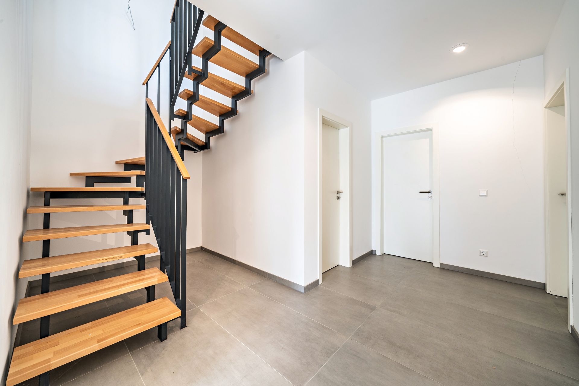 Heller Flur mit moderner Holztreppe und mehreren weißen Türen.