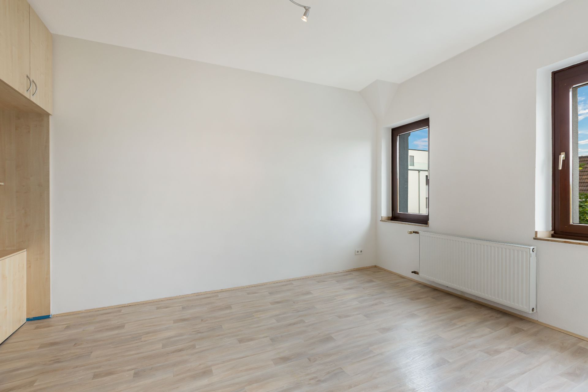 Heller leerer Raum mit zwei Fenstern, Holzfußboden und Einbauschrank.