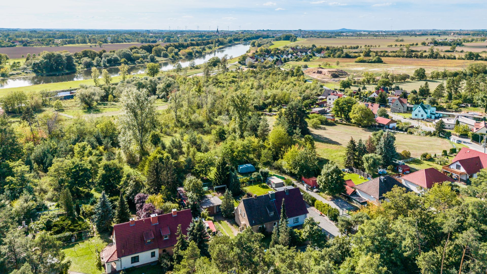 Luftaufnahme von Wohnhäusern mit Gärten und viel Grün, Fluss im Hintergrund.