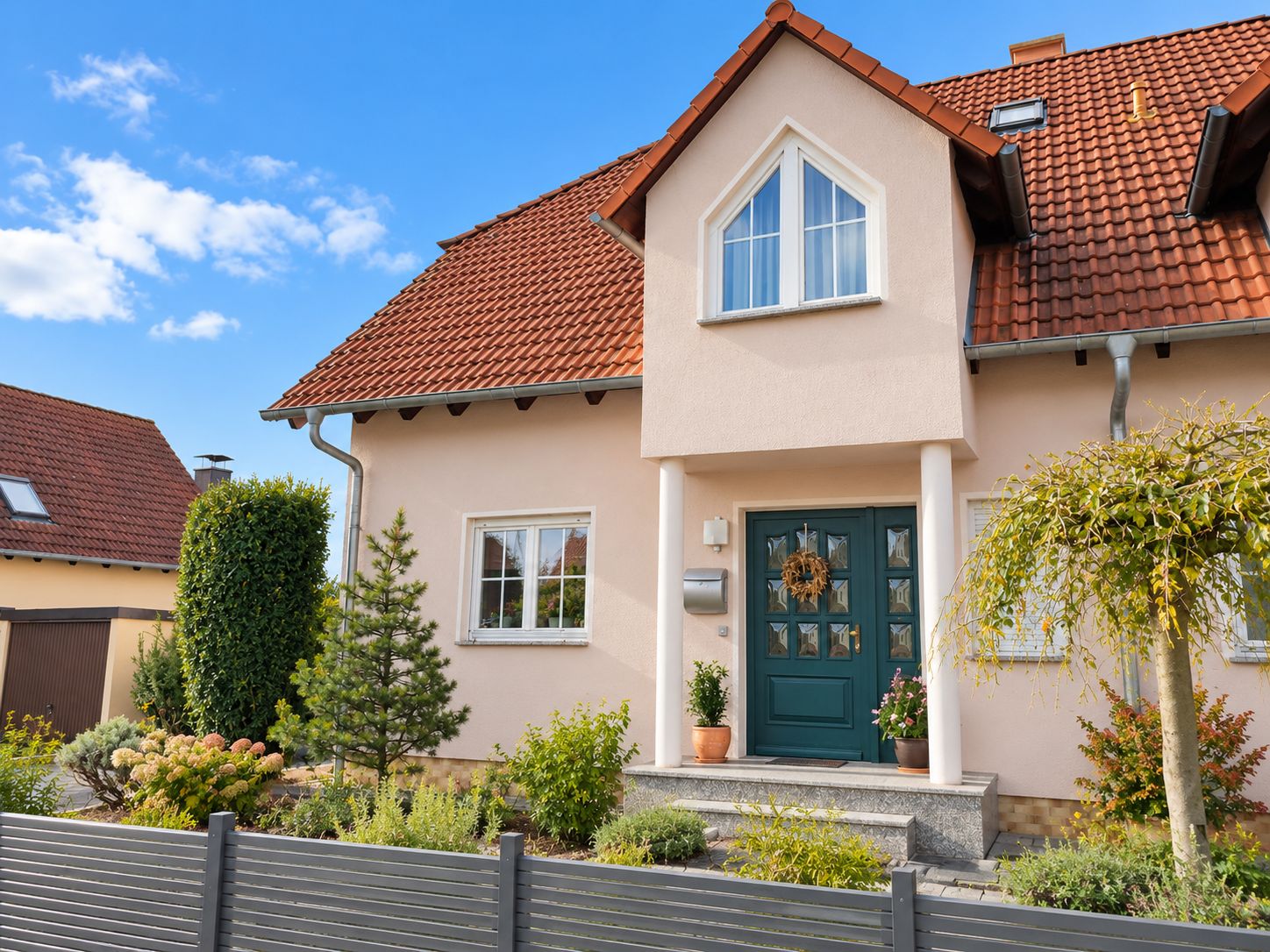 Einfamilienhaus mit rotem Dach, grünem Eingang und kleinem Vorgarten.