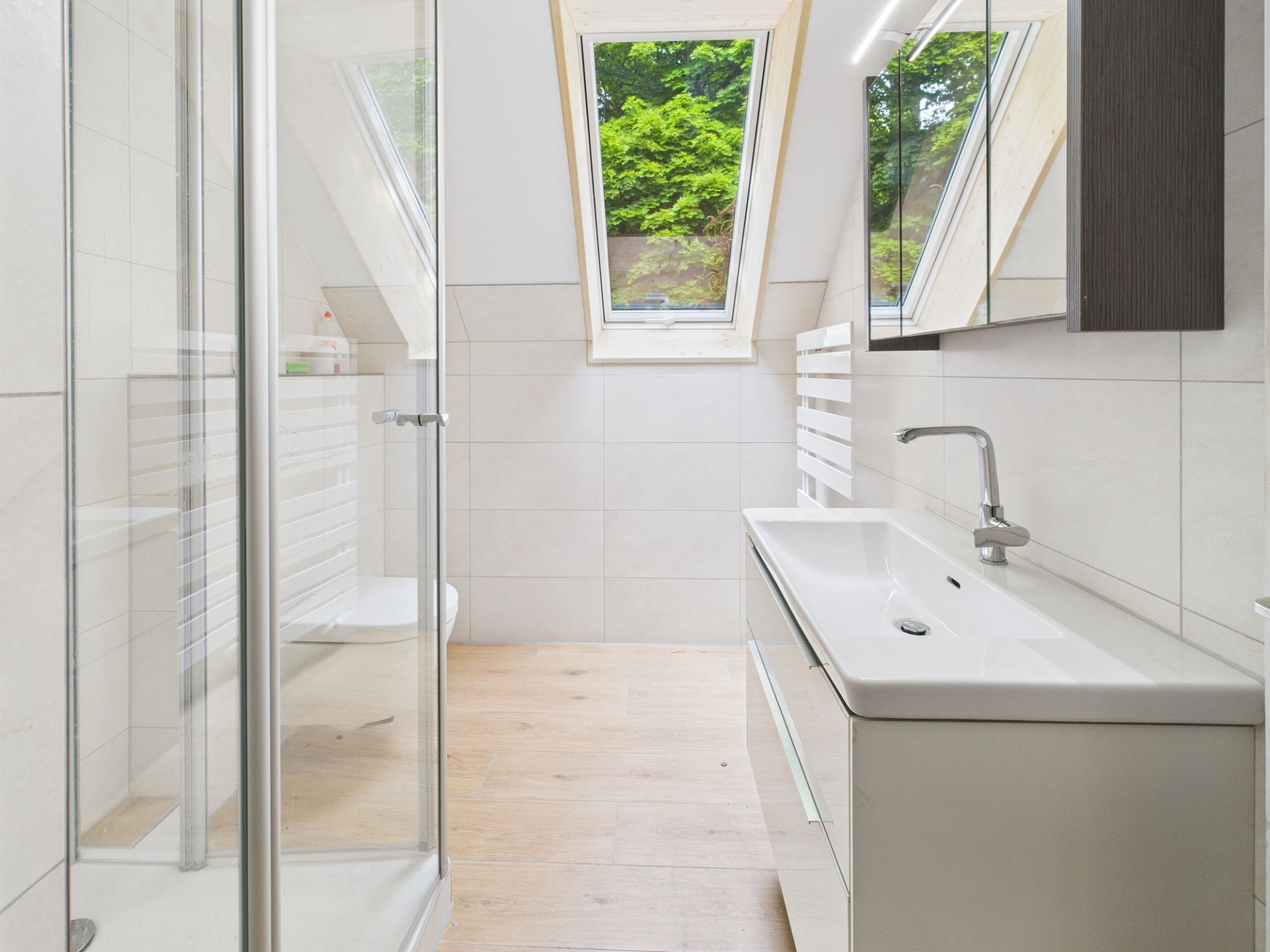 Modernes Badezimmer mit Dachfenster, Dusche, Waschbecken und Spiegel.