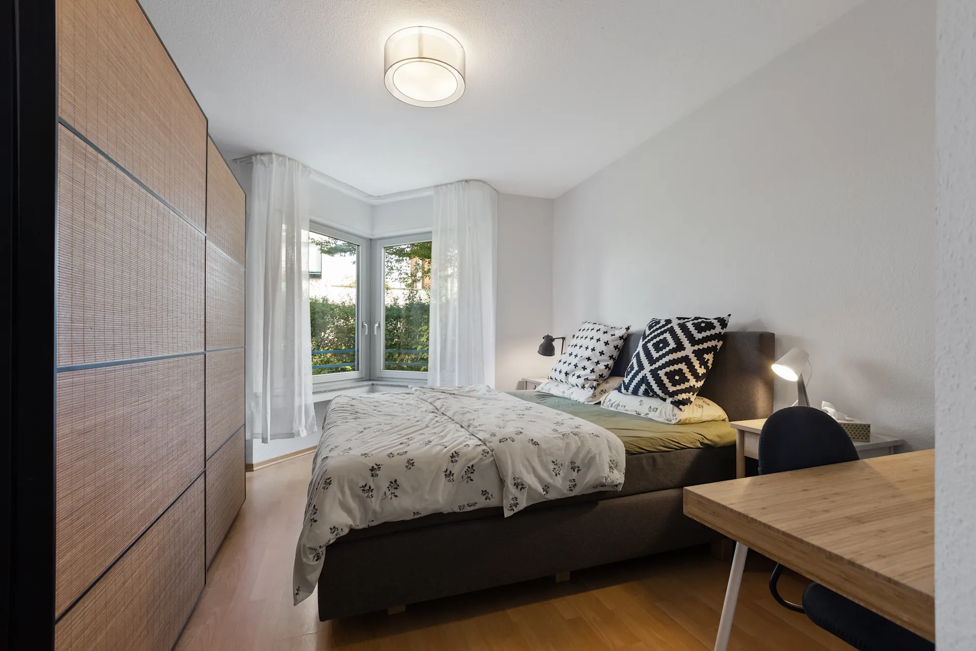 Helles Schlafzimmer mit Doppelbett, großem Fenster, Schreibtisch und Kleiderschrank.