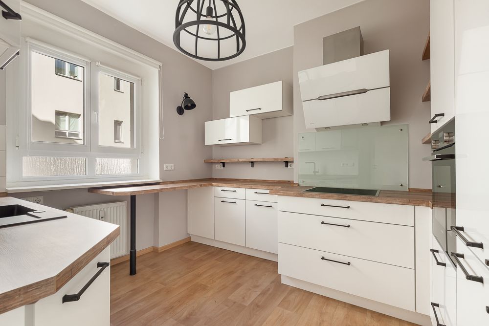 Moderne Küche mit weißen Schränken, Holzarbeitsplatten und großem Fenster.