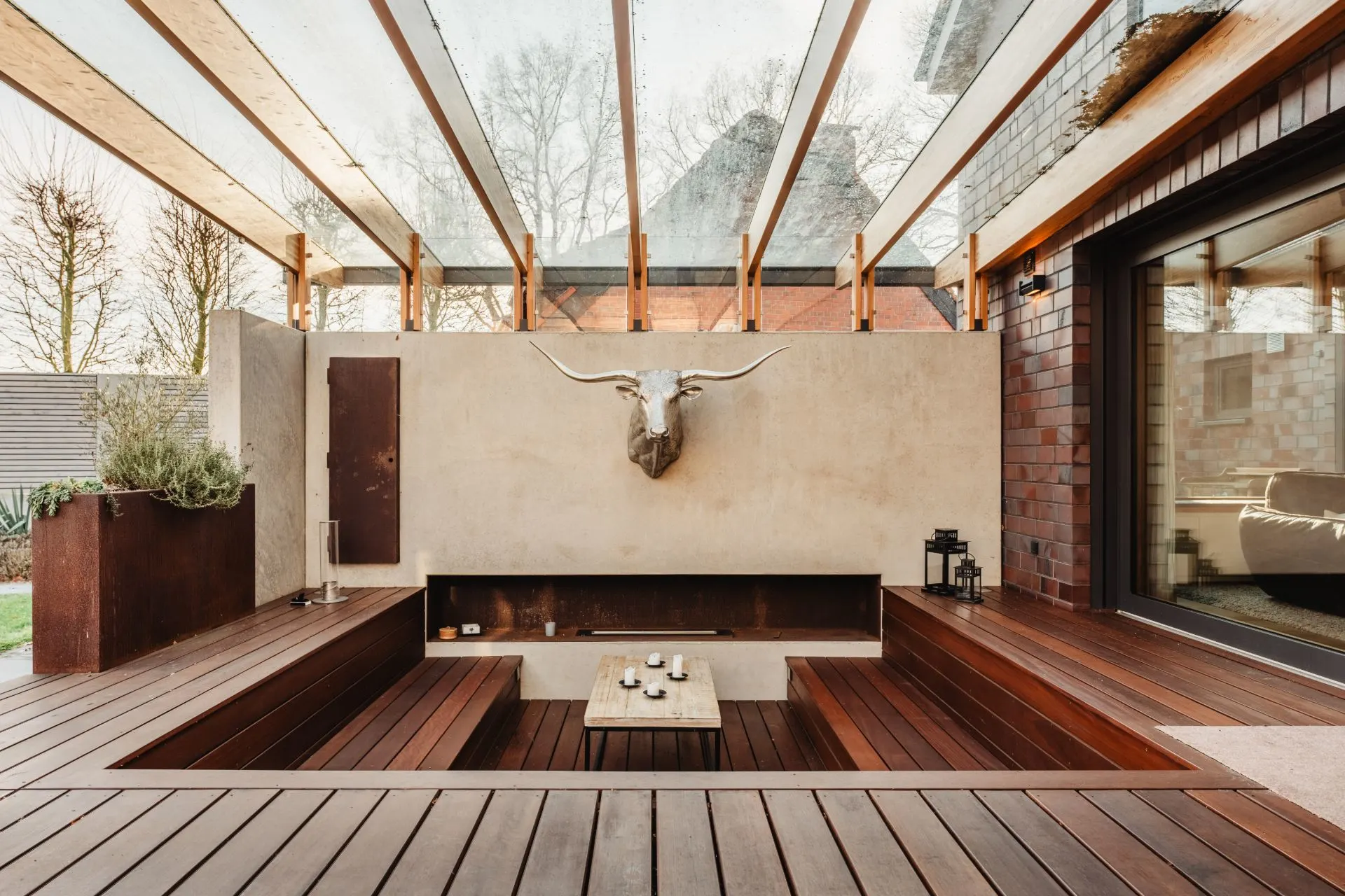 Überdachte Holzterrasse mit eingelassener Sitzecke, Tisch und Stierkopf an der Wand.