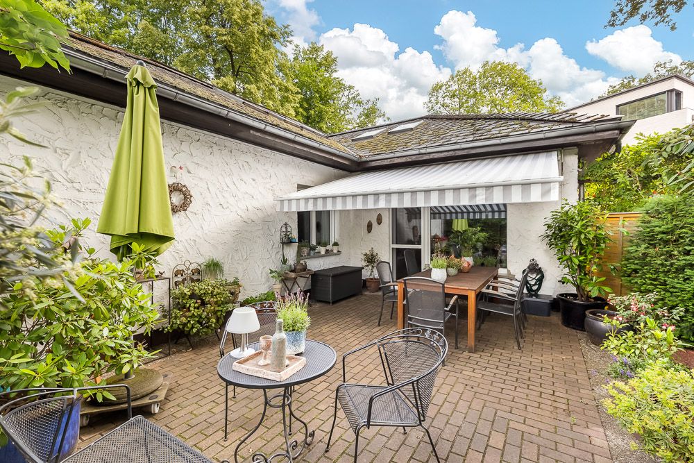 Gepflegte Terrasse mit Sitzmöbeln, Pflanzen und einer Markise an einem weißen Wohnhaus.