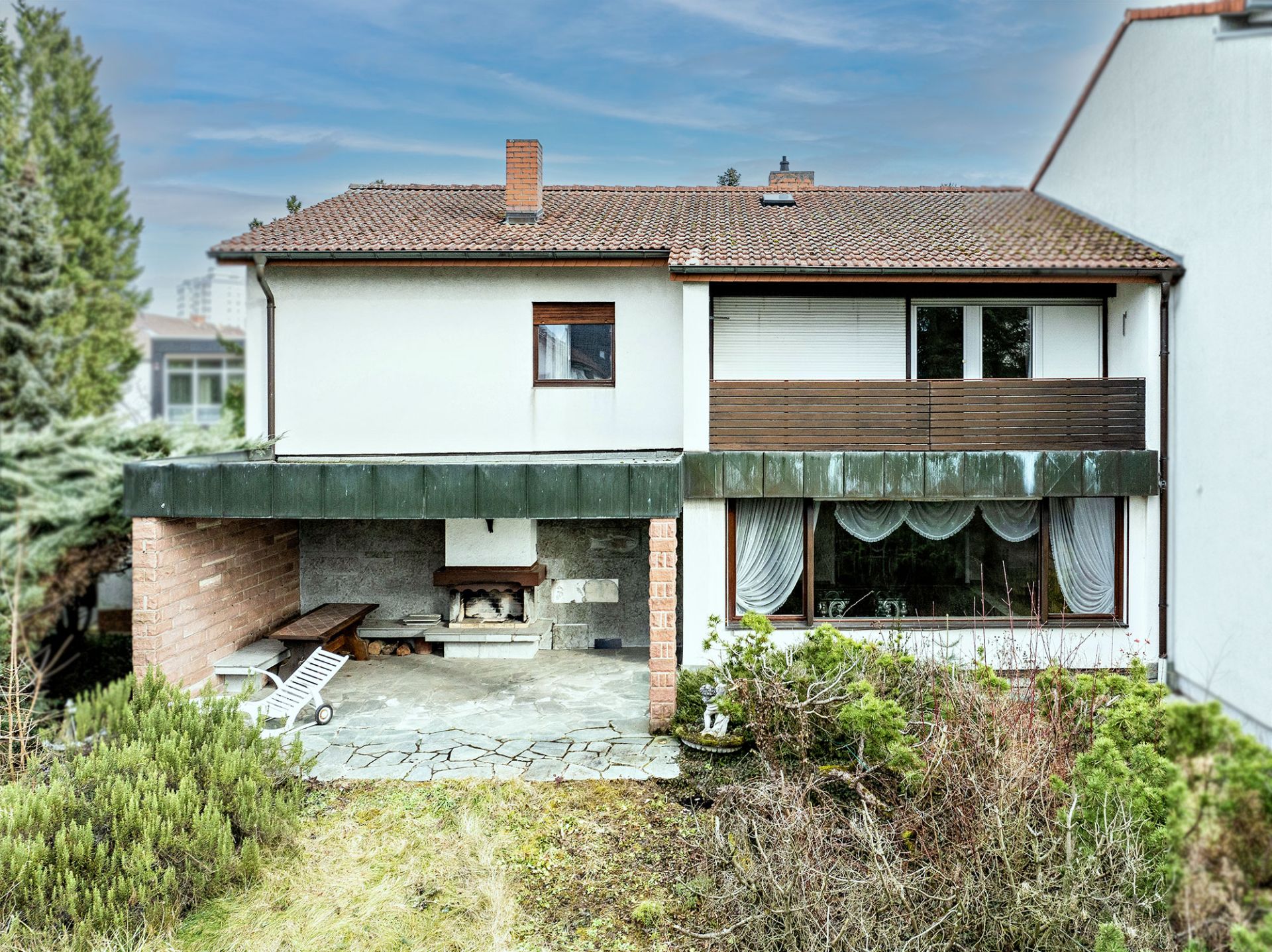 Zweistöckiges Wohnhaus mit Terrasse, Garten und großem Fenster mit Vorhängen.