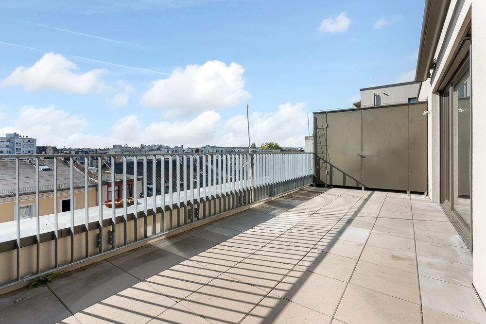 Große Dachterrasse mit heller Fliesenfläche und Metallgeländer, Blick auf umliegende Häuser.
