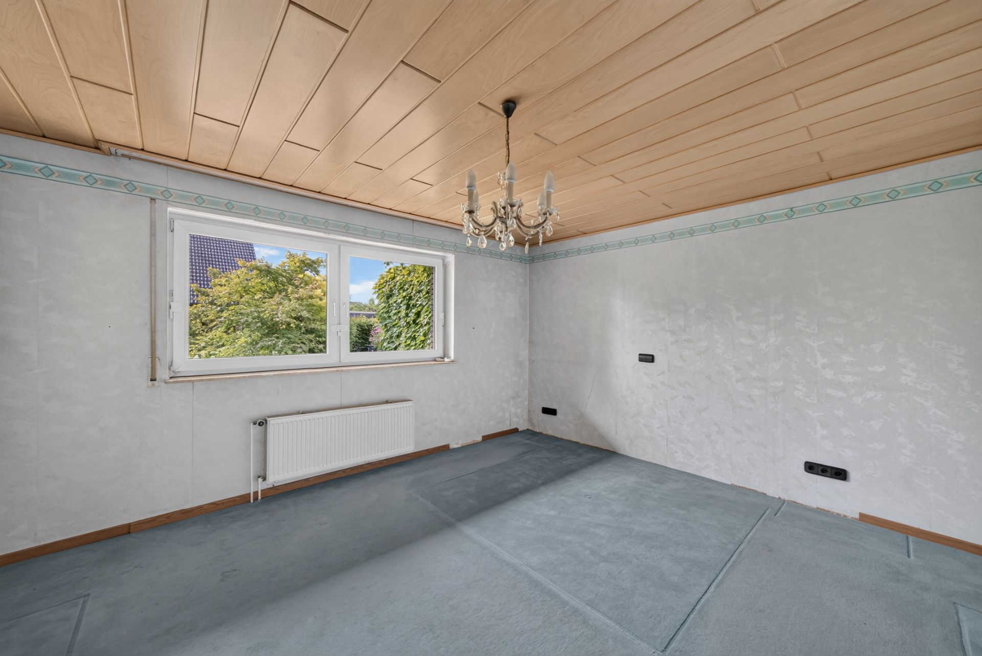 Leeres Zimmer mit Teppichboden, Holzdecke, Fenster und Kronleuchter.
