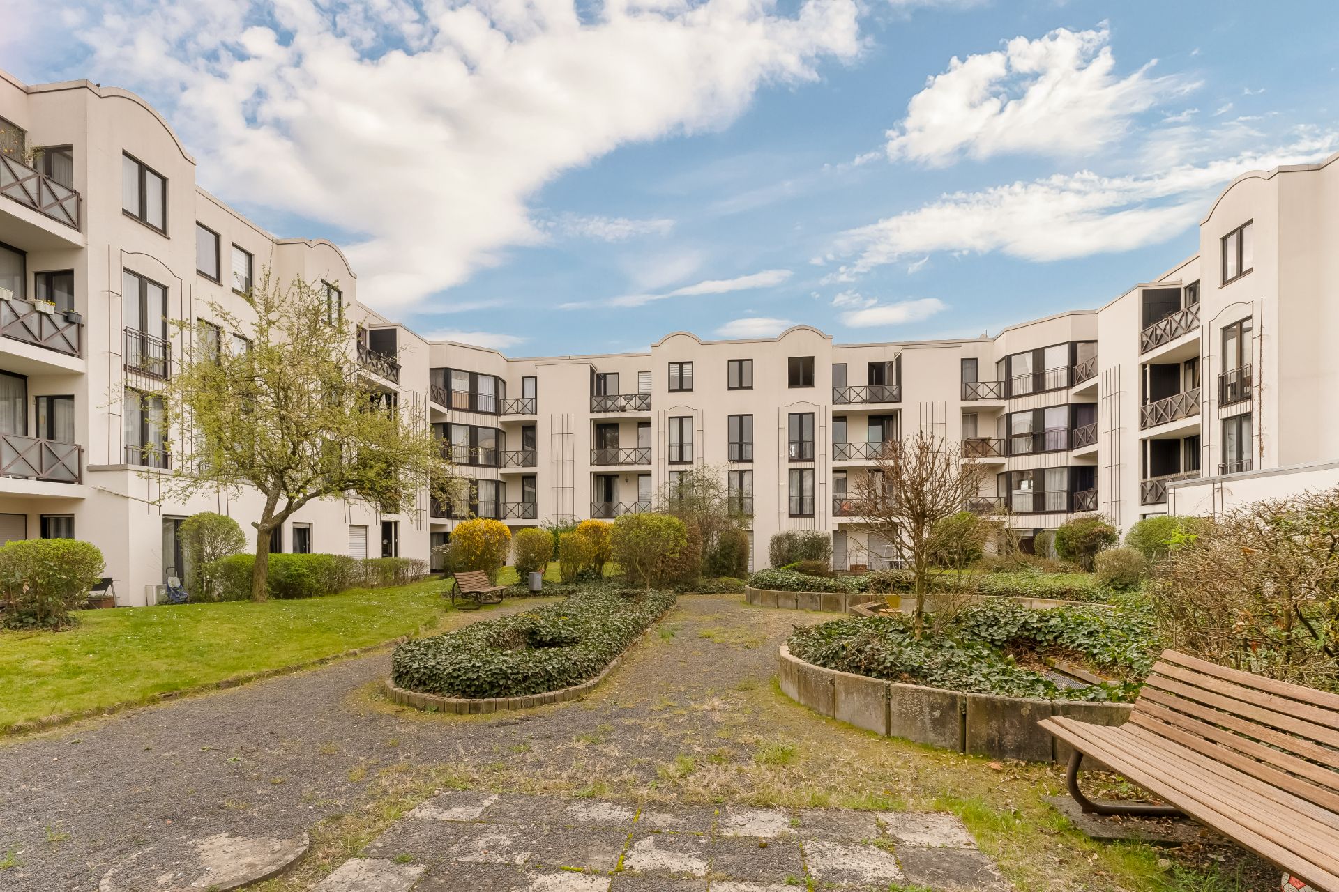 Innenhof eines Wohngebäudes mit Bänken, Wegen und bepflanzten Beeten bei Tageslicht.