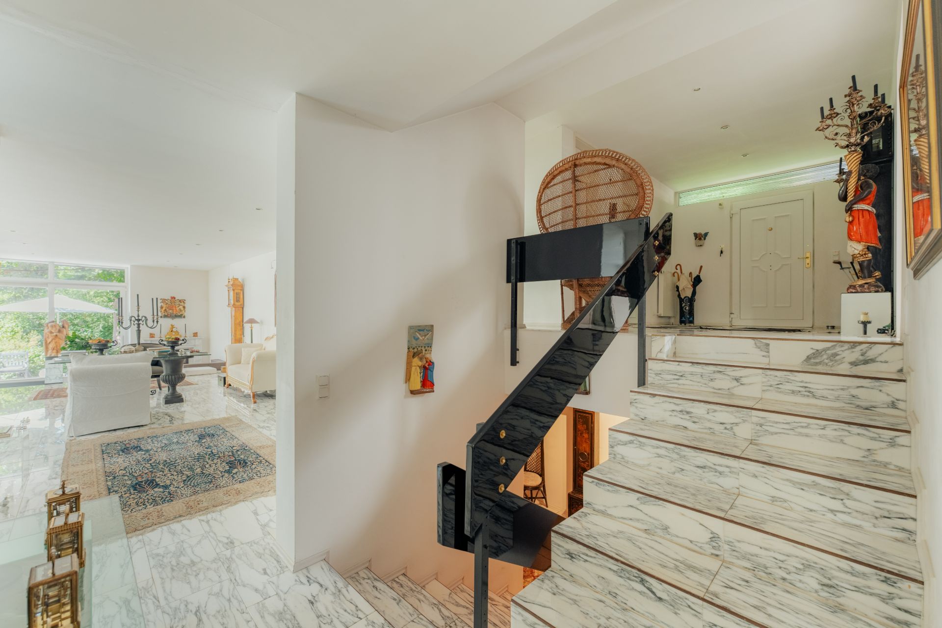Heller Wohnbereich mit Marmortreppe, dekorativen Figuren und großem Fenster im Hintergrund.