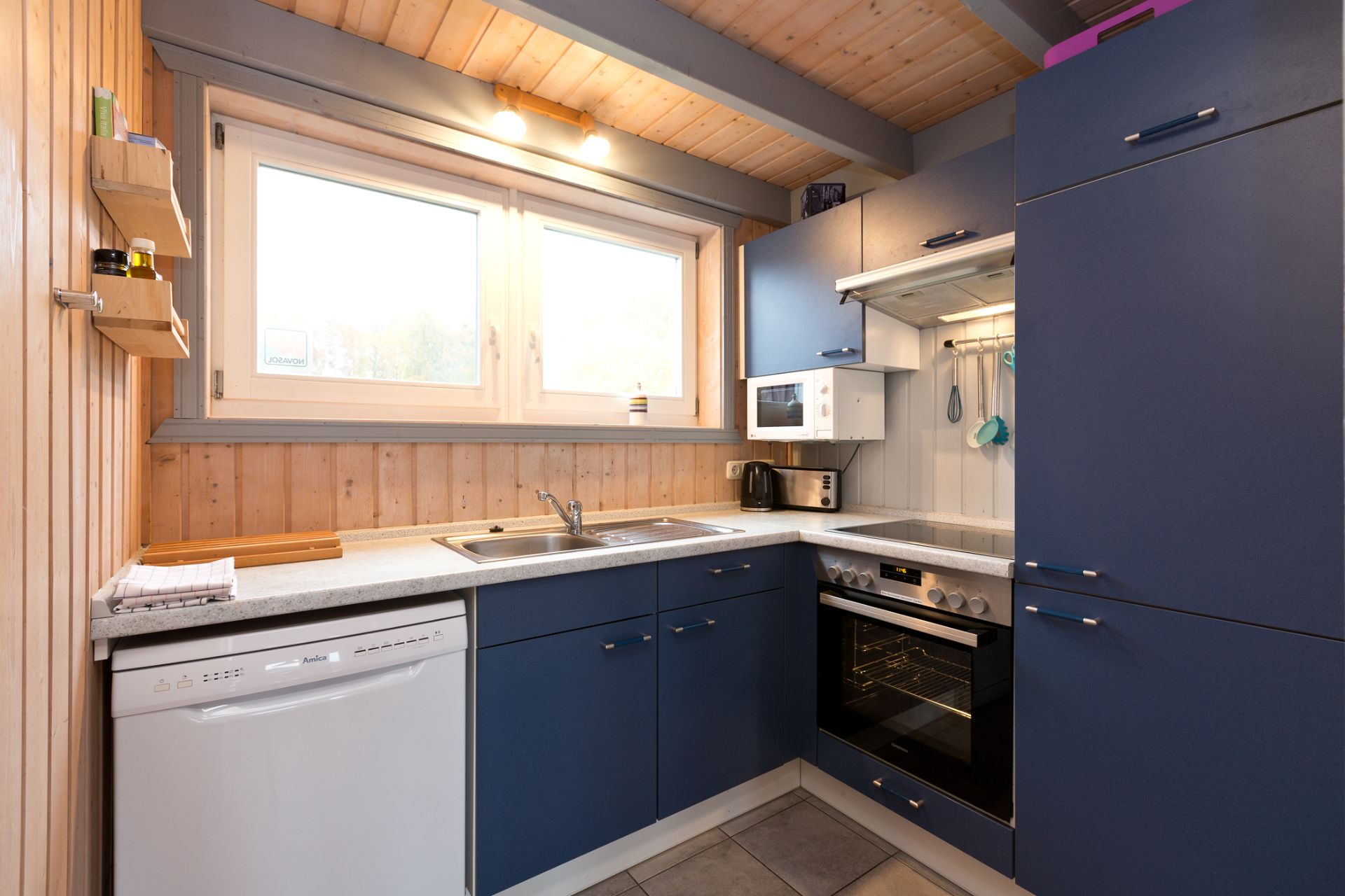 Moderne Küche mit blauen Schränken, Herd, Spülmaschine und großem Fenster.