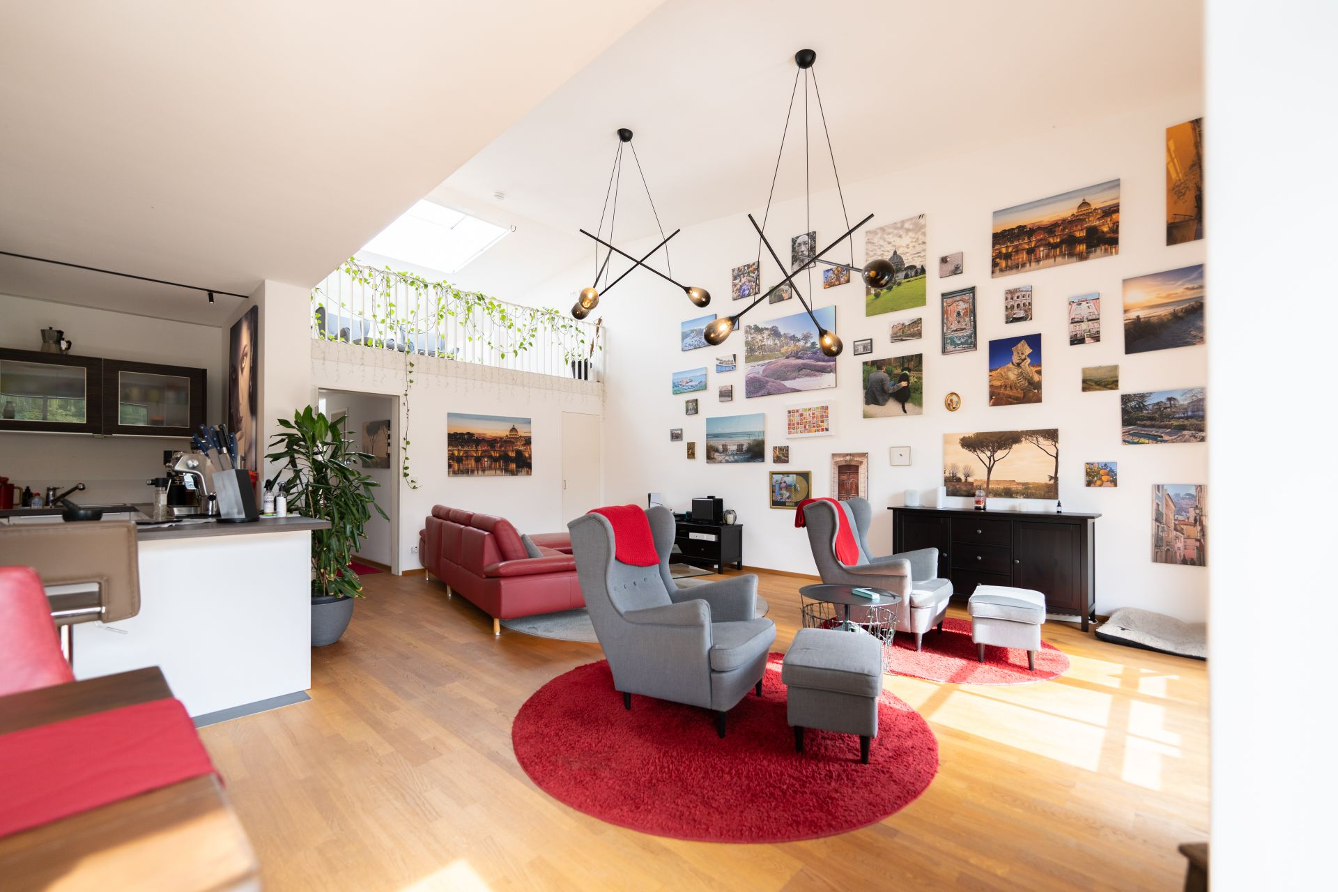 Helles Wohnzimmer mit roten Sofas, Sesseln, Holzboden und vielen Bildern an der Wand.